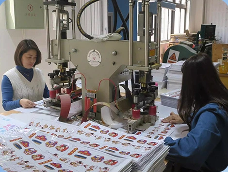 Workers handling printed sticker sheets at production presses