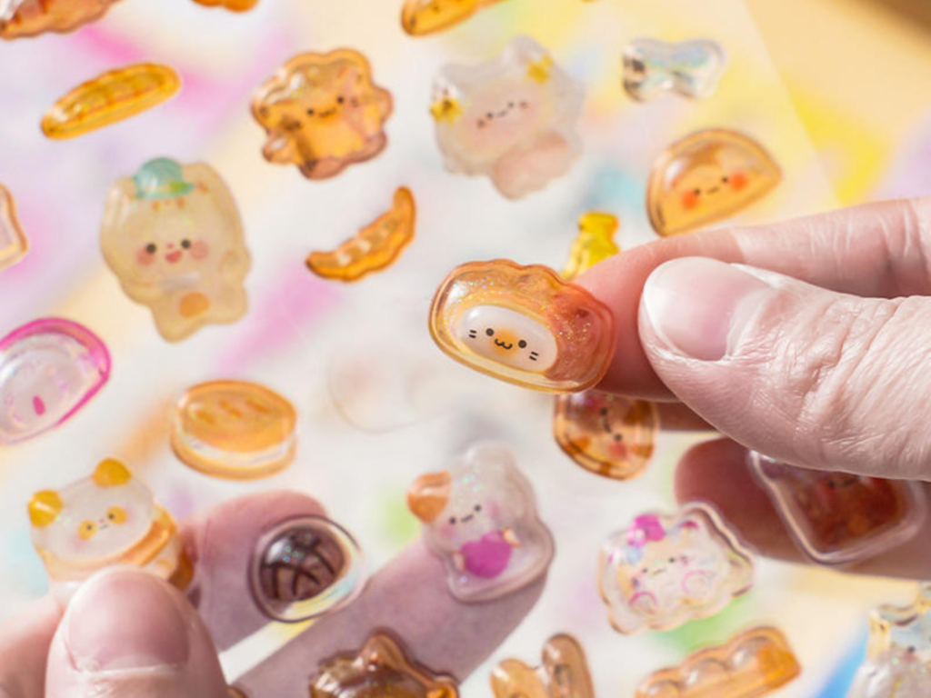 Hand peeling a small 3D bubble sticker from an illustrated sheet