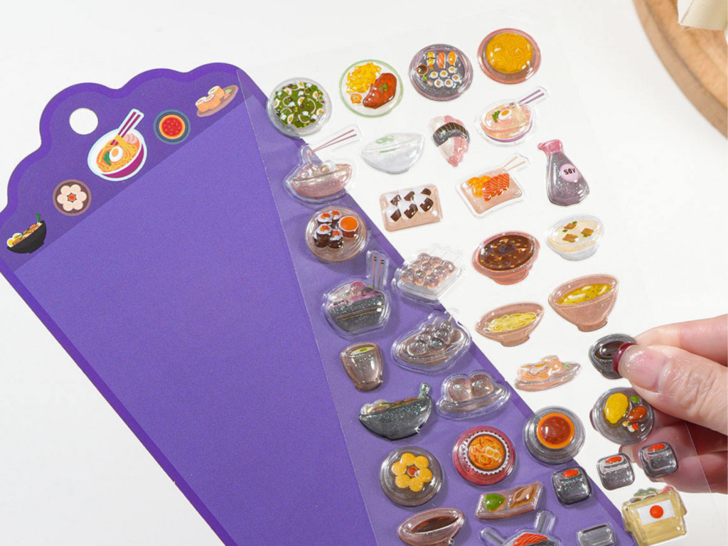 Hand holding a food-themed 3D bubble sticker sheet beside a purple backing card